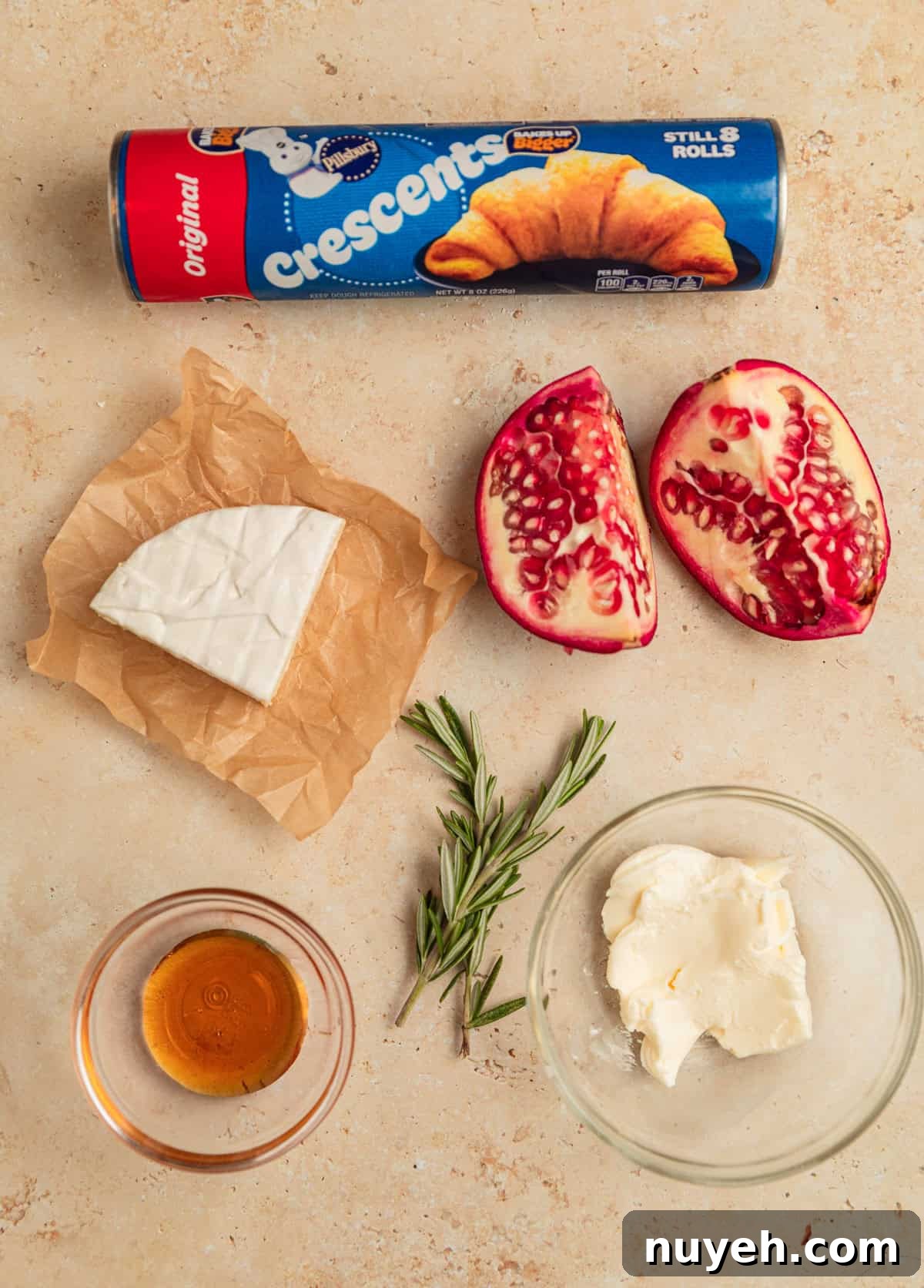 Crescent roll package, wedge of brie, rosemary sprigs and other ingredients on surface.
