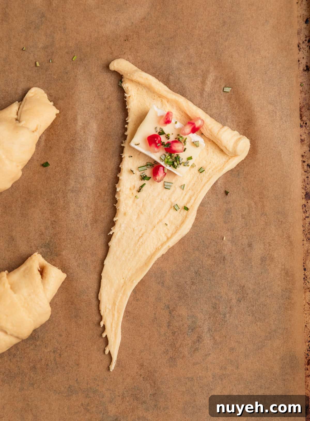 Crescent roll dough on parchment with brie, rosemary and pomegranate.