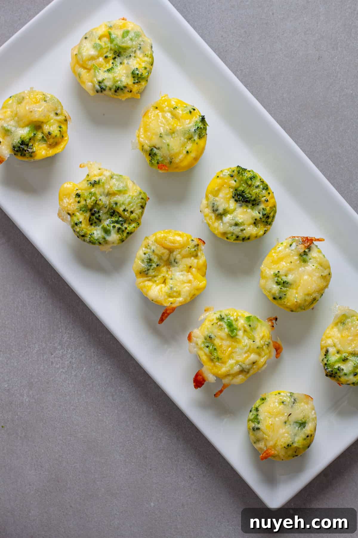 A tray of mini broccoli and cheddar egg bites on a gray table.