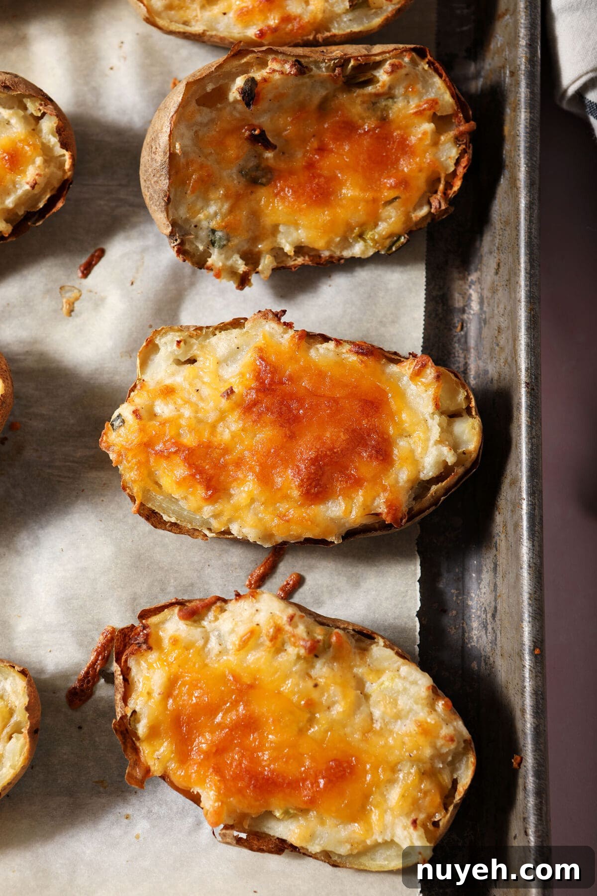Twice baked potatoes covered in gooey cheese on a sheet pan after baking