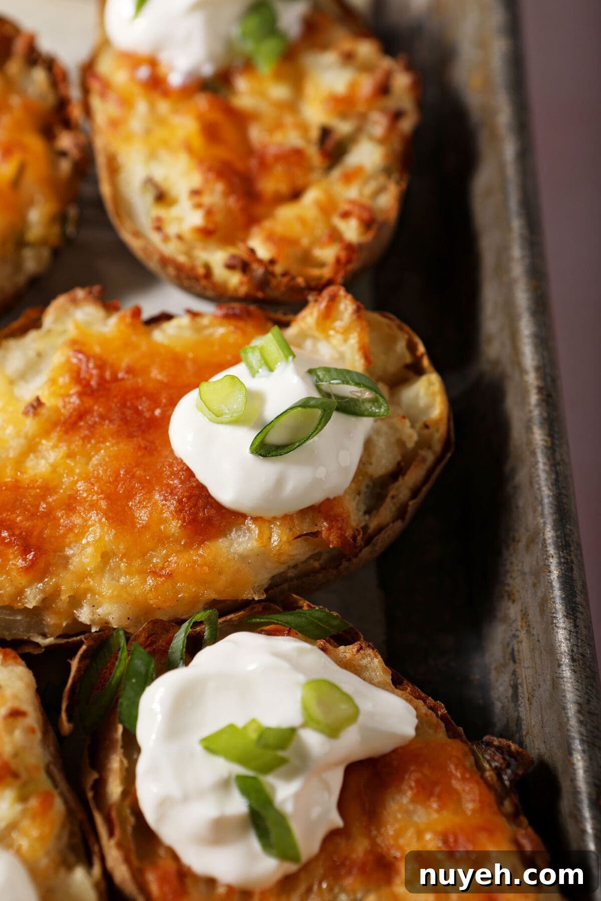 Close up of a few twice baked potatoes on a metal pan garnished with sour cream and scallions