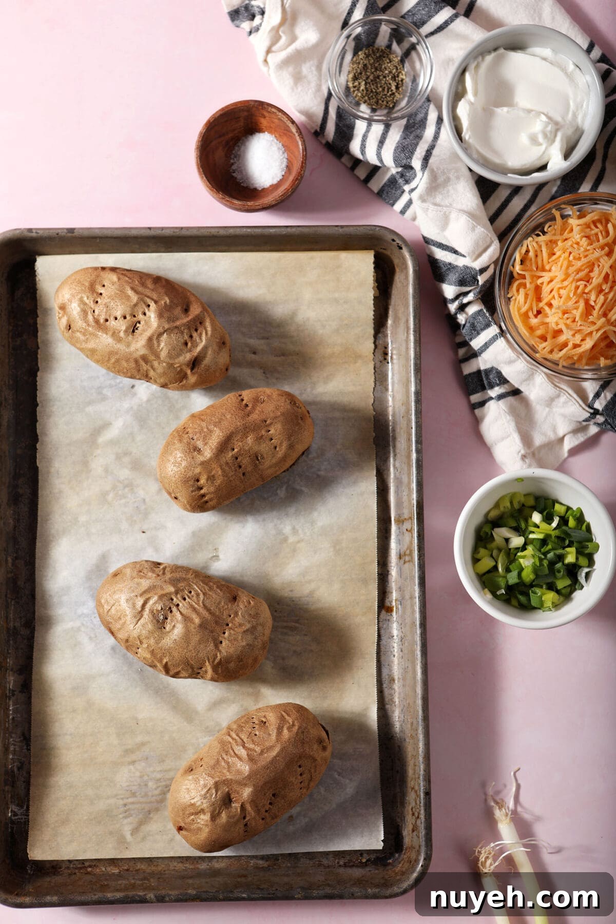 Baked potatoes on a sheet pan surrounded by twice baked potato ingredients