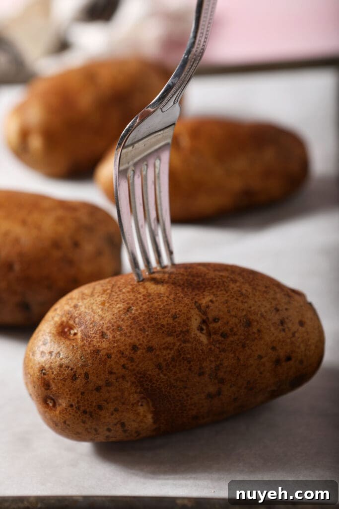 A fork pierces a potato on a sheet pan