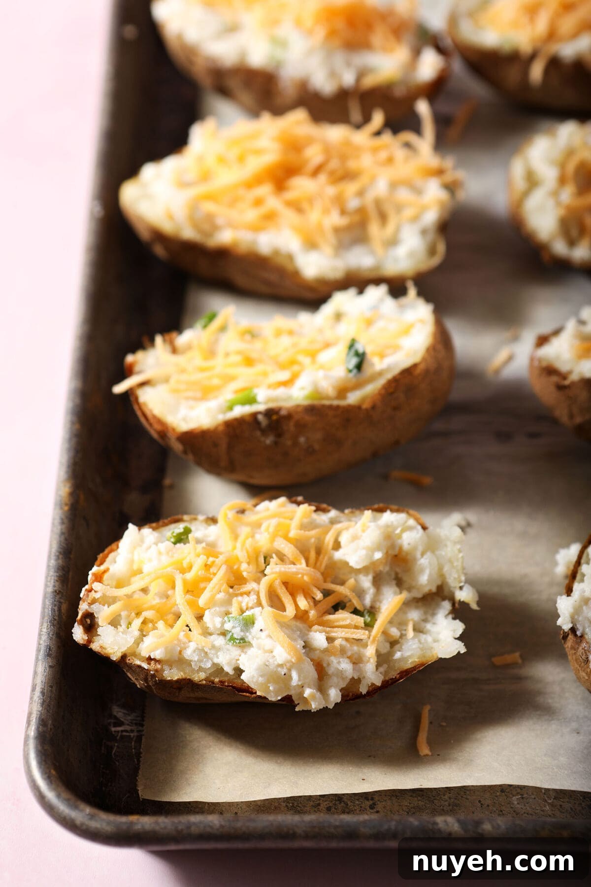 Twice baked potatoes topped with shredded cheese on a pan before baking