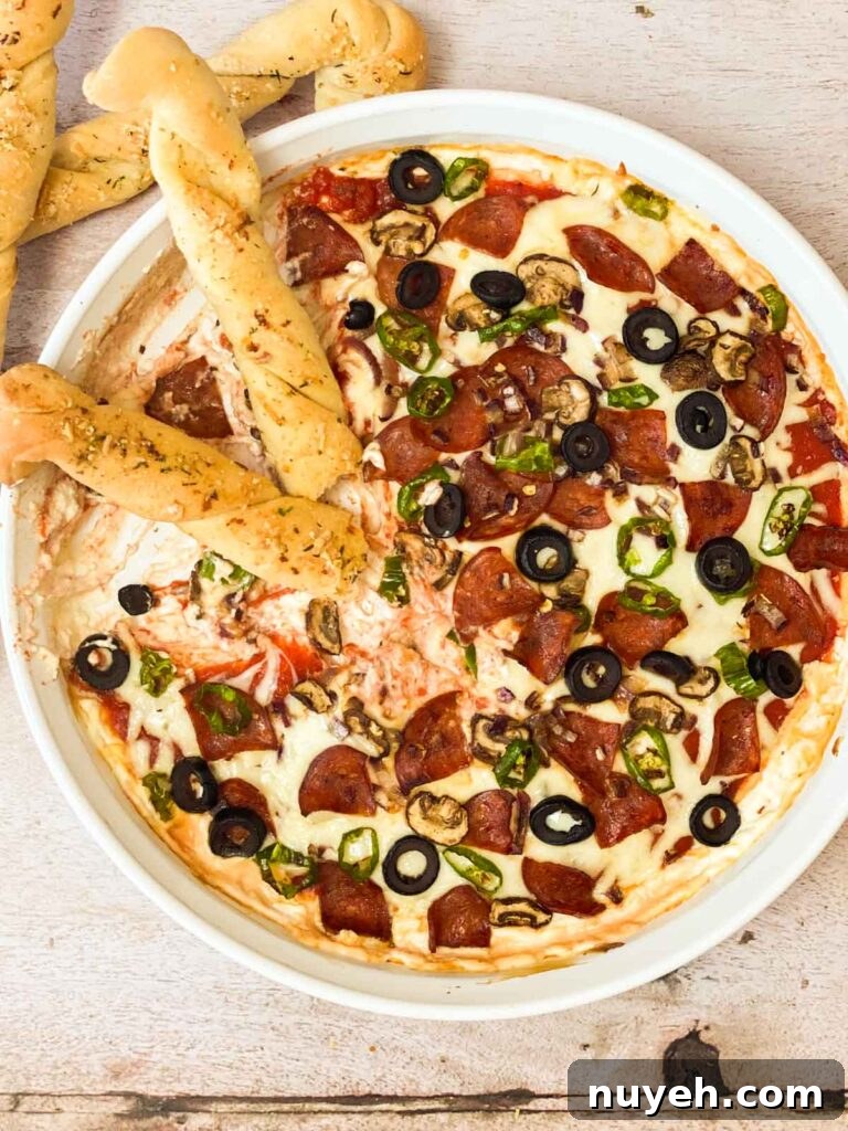 A top down view of half eaten pizza dip with breadsticks dipped into it.