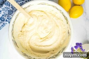 A bowl with a well-mixed, smooth lemon bread batter, a wooden spoon resting inside, ready to be poured into a loaf pan.