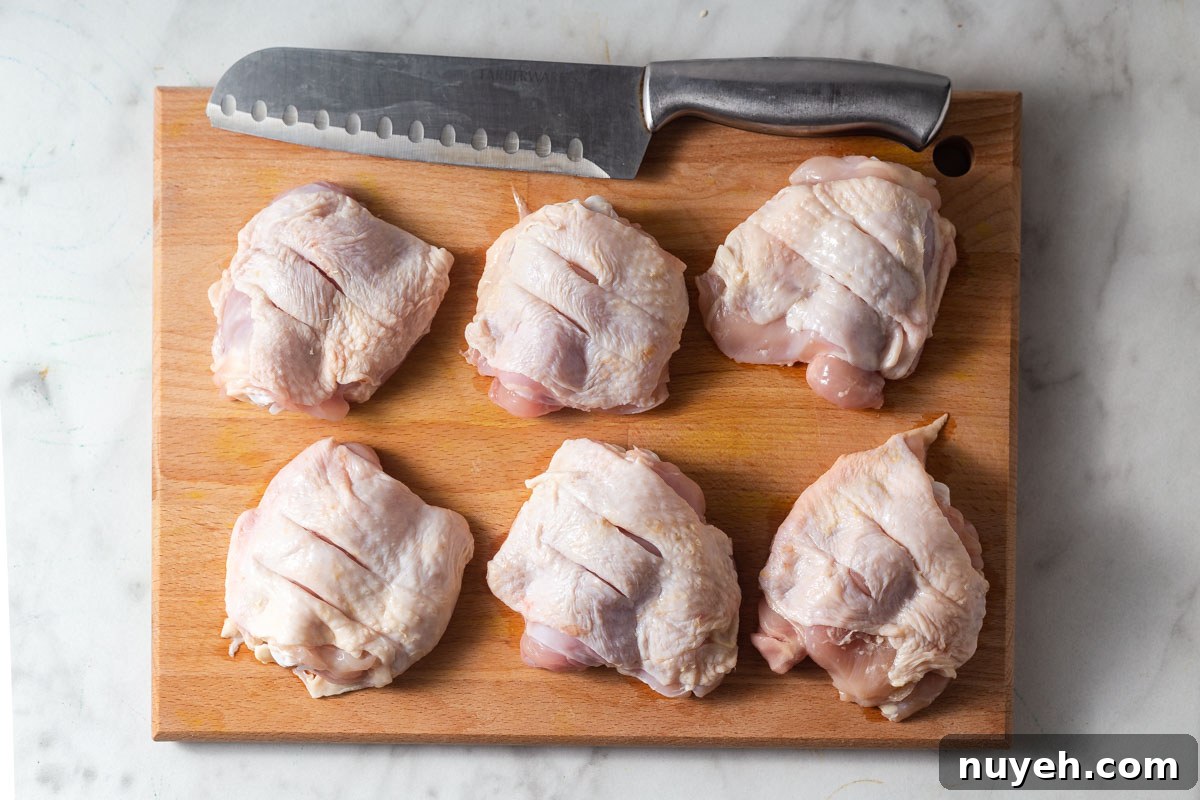 scored chicken thighs on a chopping board with a knife.