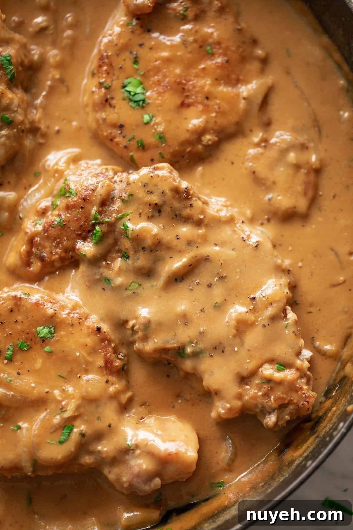 Top view of Smothered Pork Chops cooked in a black skillet garnished with fresh chopped parsley.