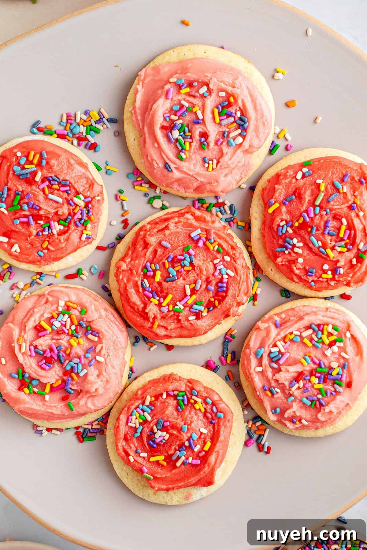 Classic Frosted Sugar Cookies Recipe 2 Gray plate with pink frosted sugar cookies with sprinkles. Top view.