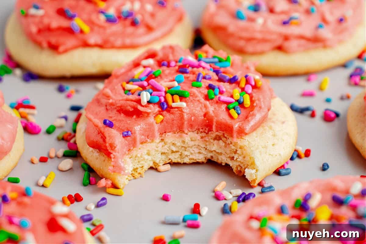 Classic Frosted Sugar Cookies Recipe 12 Bitten pink-frosted sugar cookie with sprinkles. Light gray surface, more cookies.