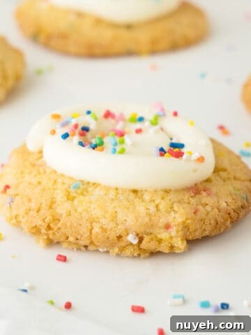 Classic Frosted Sugar Cookies Recipe 14 Close up of funfetti cookie with frosting. White surface with sprinkles.
