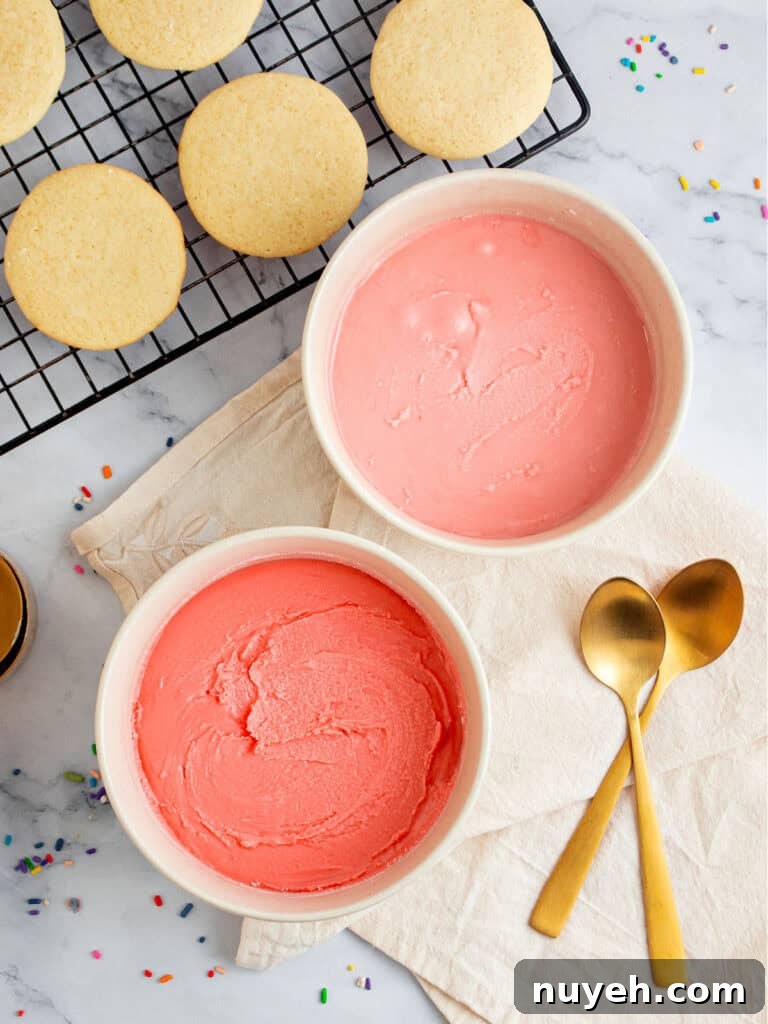 Classic Frosted Sugar Cookies Recipe 8 White bowls with pink buttercream, gold spoons, wire rack with cookies. Marbled surface.