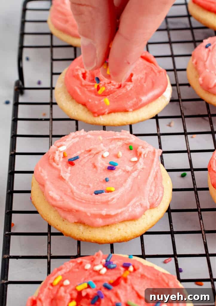 Classic Frosted Sugar Cookies Recipe 10 Sprinkling jimmies on pink frosted cookies on a wire rack.