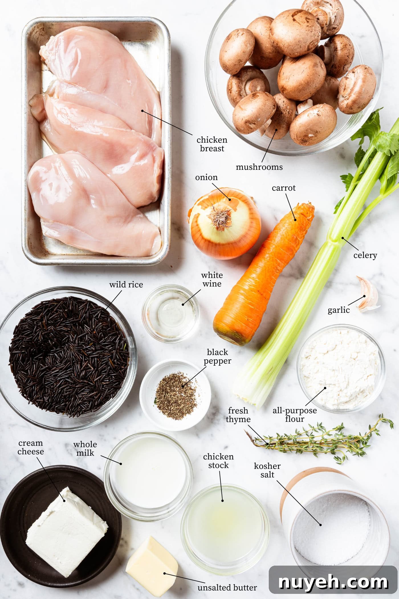 Creamy Chicken and Wild Rice Soup Recipe 4 White marble surface filled with ingredients for chicken wild rice soup including raw chicken breast, vegetables, rice, spices, and more.