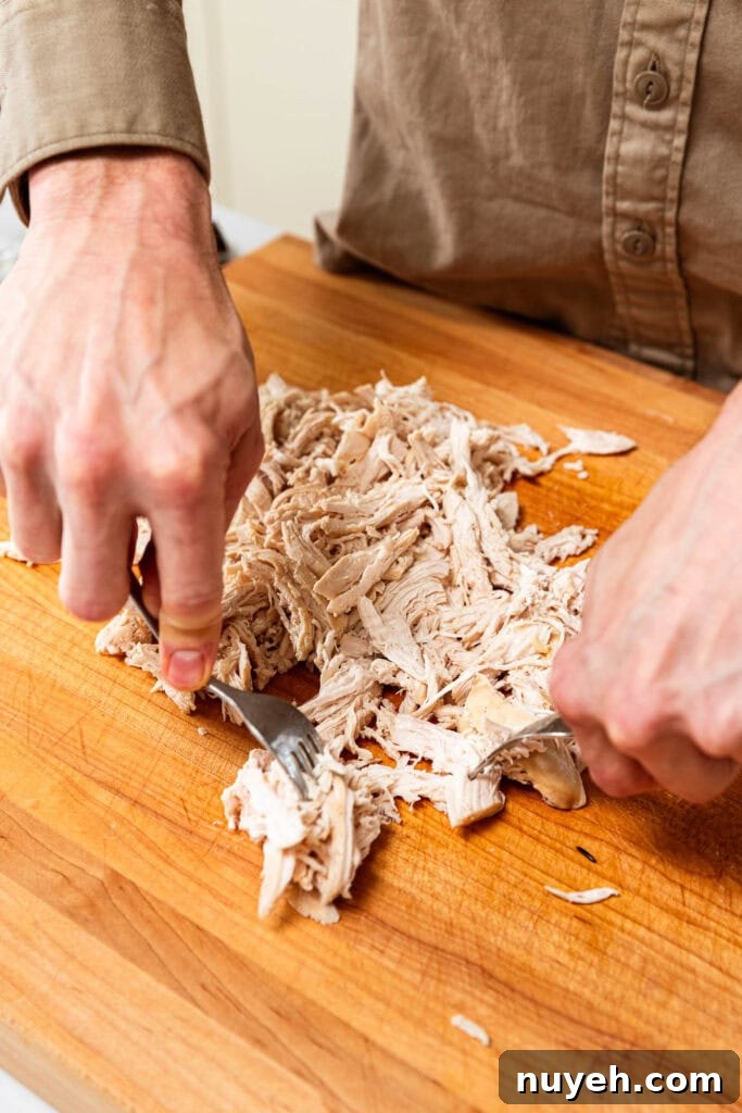Creamy Chicken and Wild Rice Soup Recipe 10 Shredding chicken by hand on a cutting board.