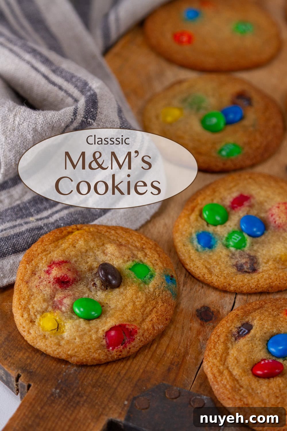 M&M's cookies on a wooden serving board with a cloth napkin in the upper left.