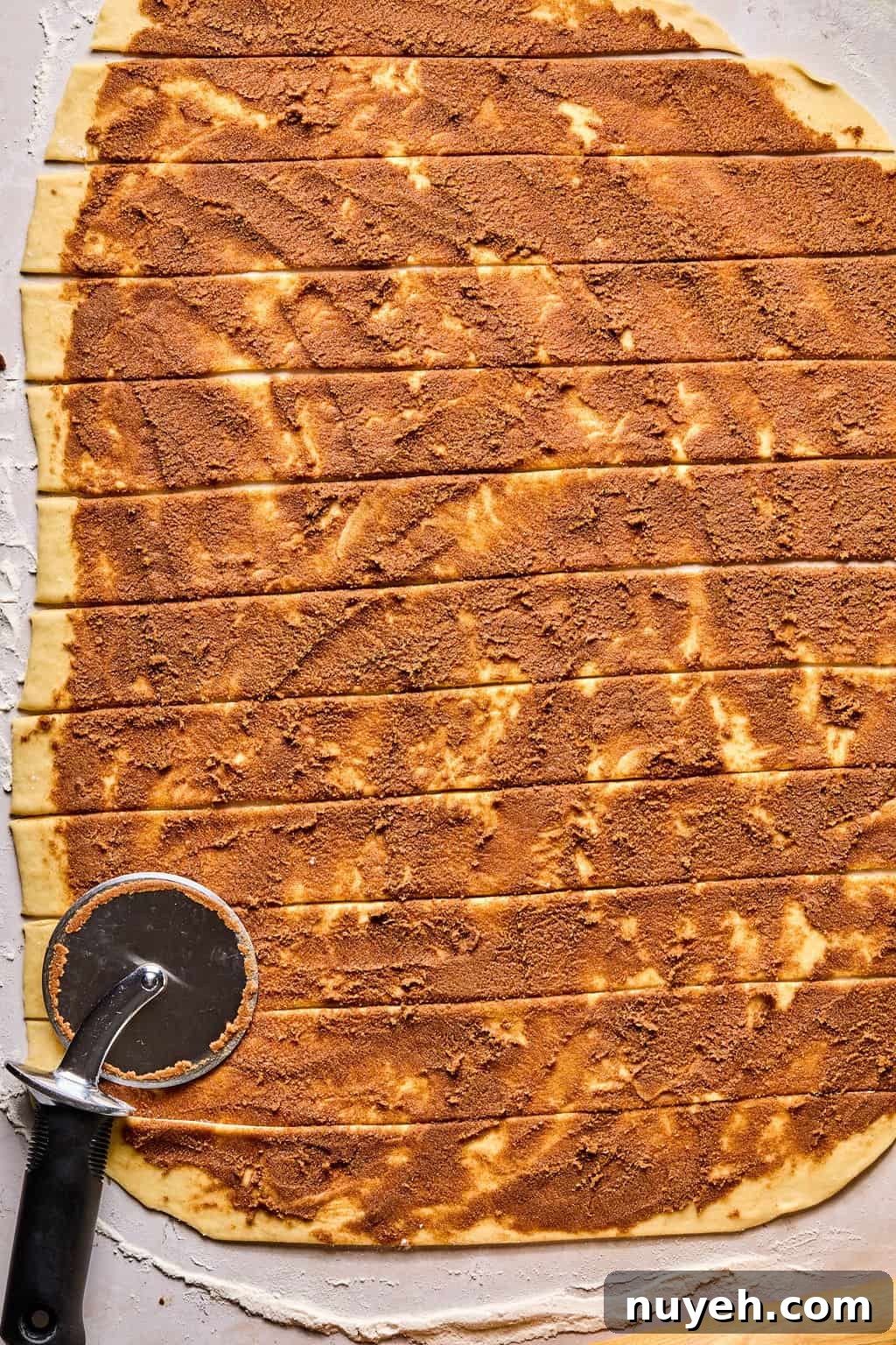 cinnamon roll dough rolled into a large rectangle and coated with cinnamon filling then cut into strips.