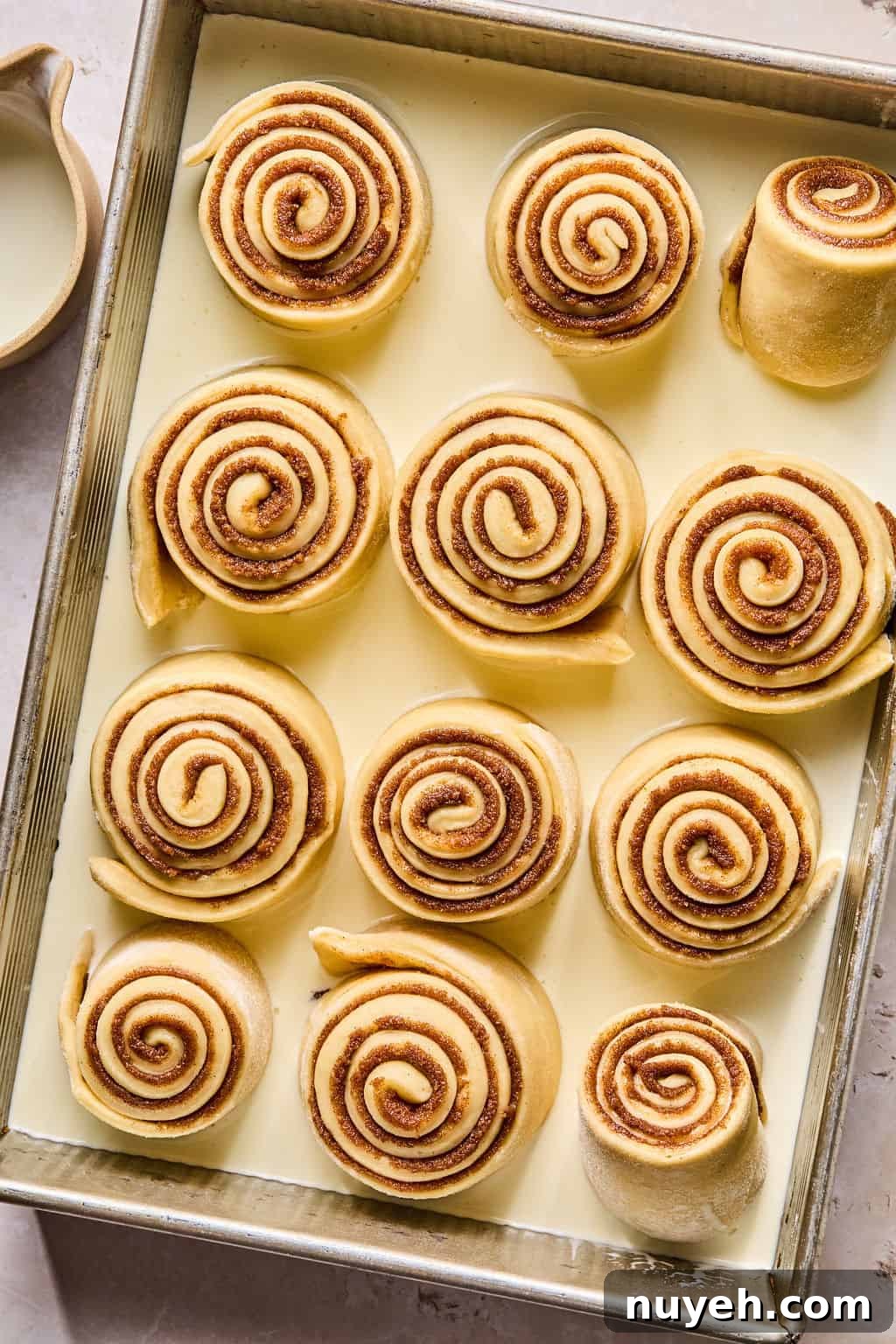 unbaked cinnamon rolls in a baking dish with heavy cream all around them.