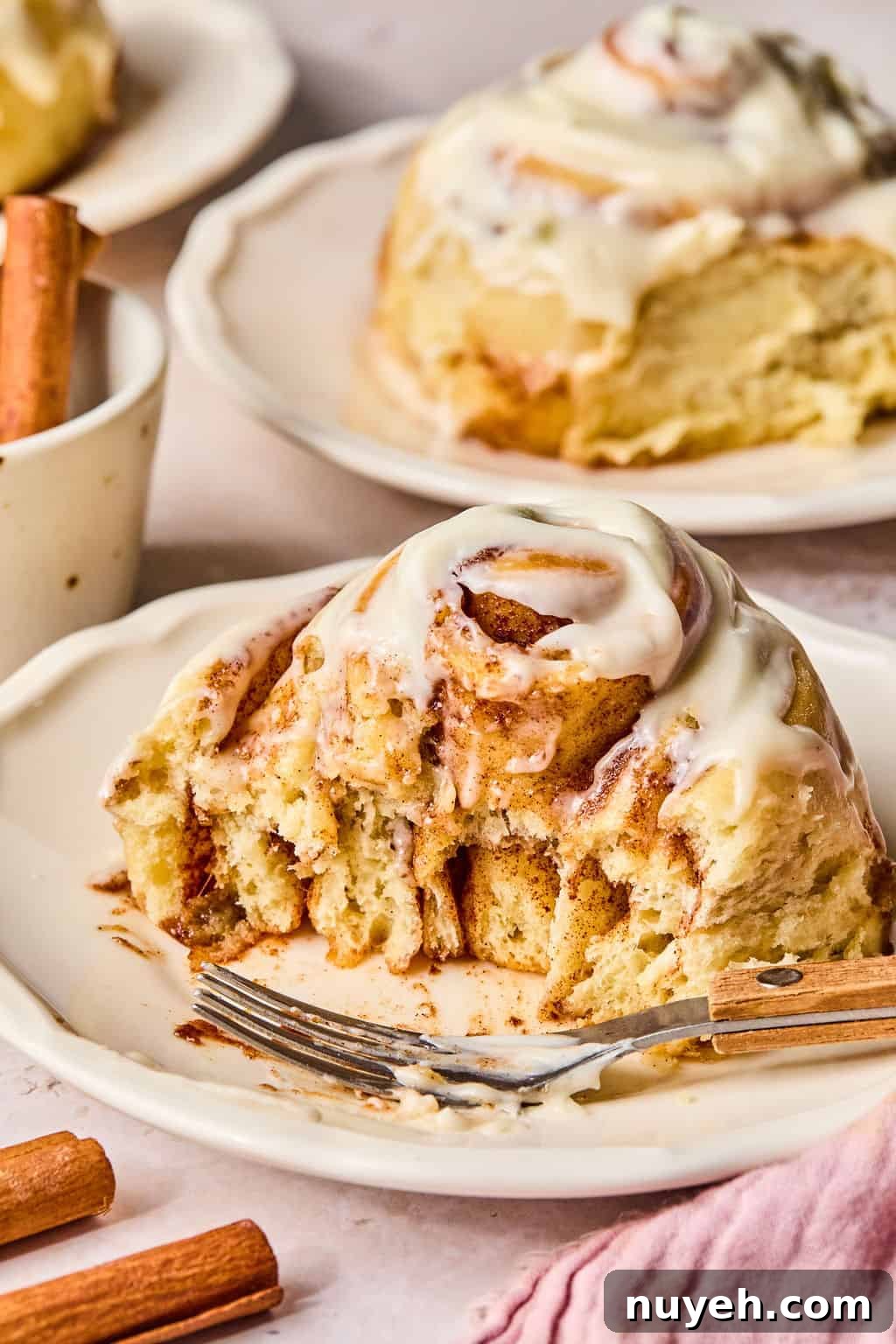 a cinnamon roll on a plate with a piece missing to see the soft and gooey center.
