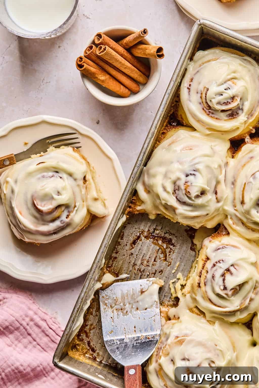 a pan of big gooey and soft cinnamon rolls with one on a plate next to the pan.