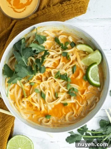 thai red curry noodles in a white bowl garnished with limes.
