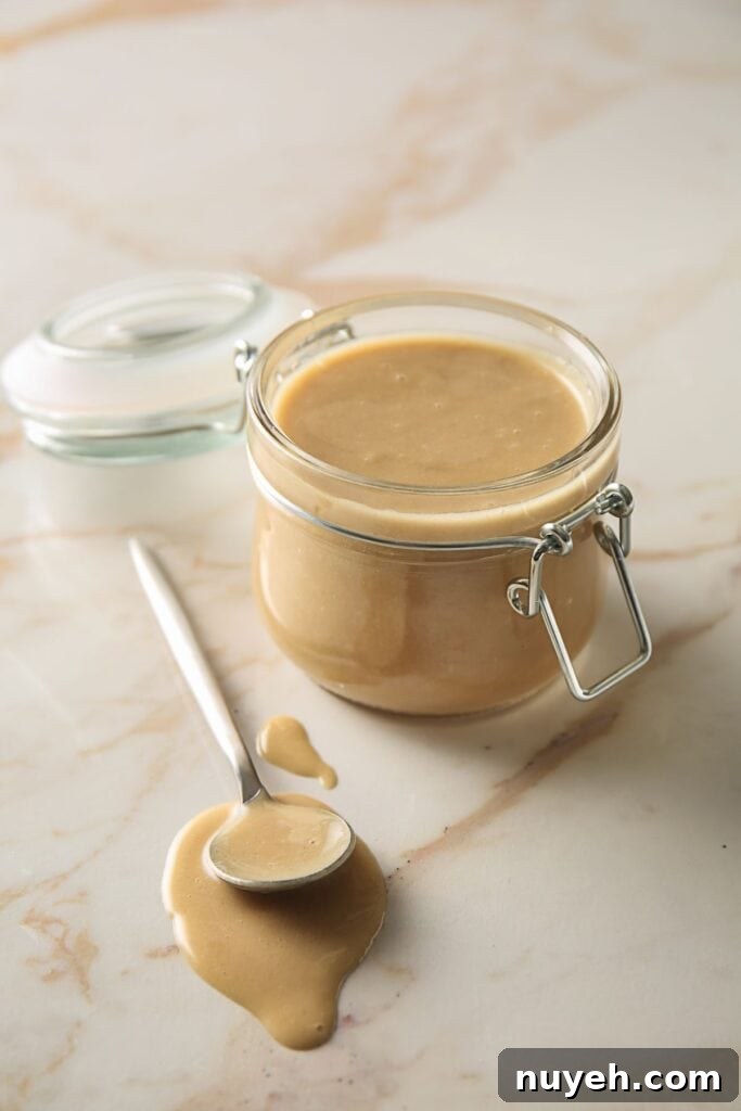 tahini in a jar with a spoon next to it.