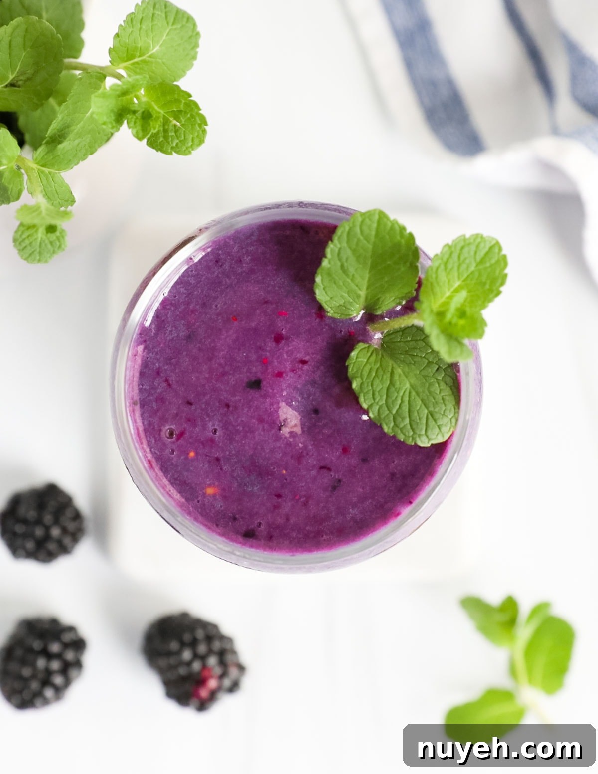 A clear cup with a purple smoothie inside and fresh mint leaves on top of the smoothie.