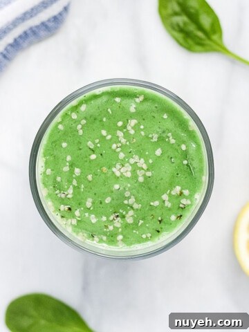 A green smoothie in a clear glass, garnished with white hemp seeds.
