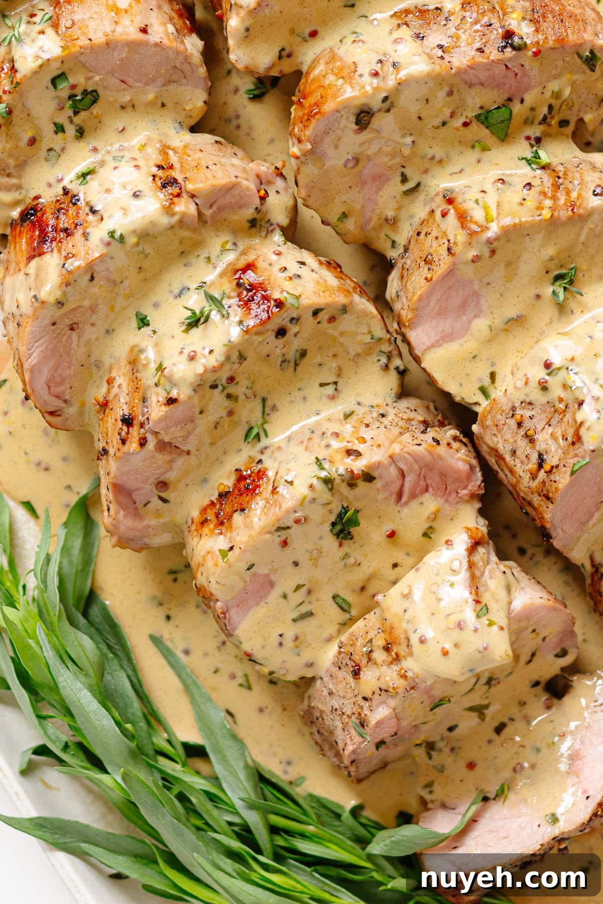 Sliced pork tenderloin with mustard sauce and a sprig of fresh tarragon.