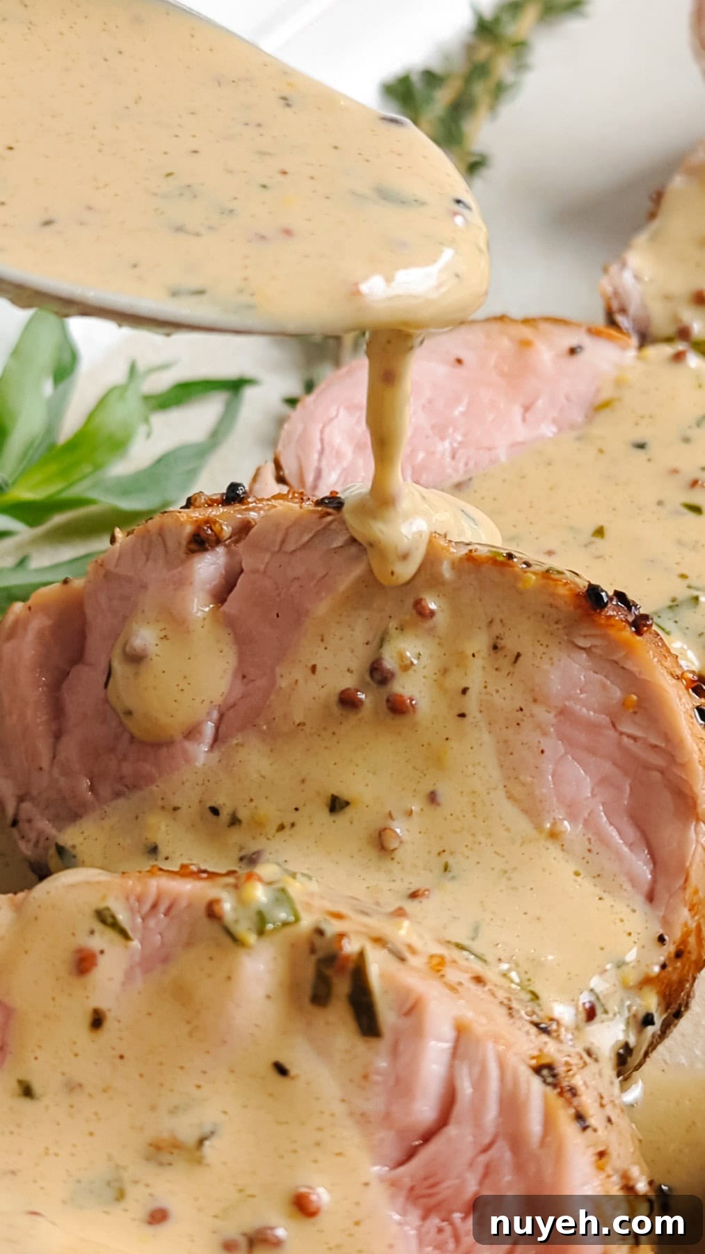 Spoon drizzling dijon cream sauce over slices of pork tenderloin.