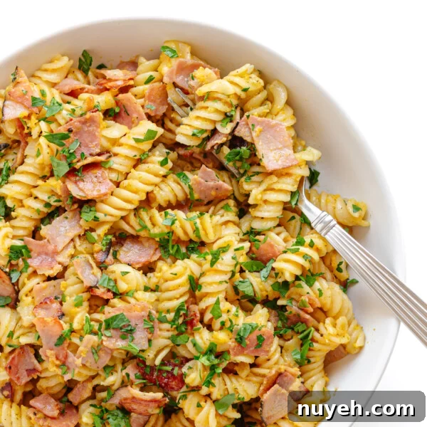 Closeup of a bowl of Schinkennudeln (German Ham and Egg Pasta) with a fork scooping out a bite.
