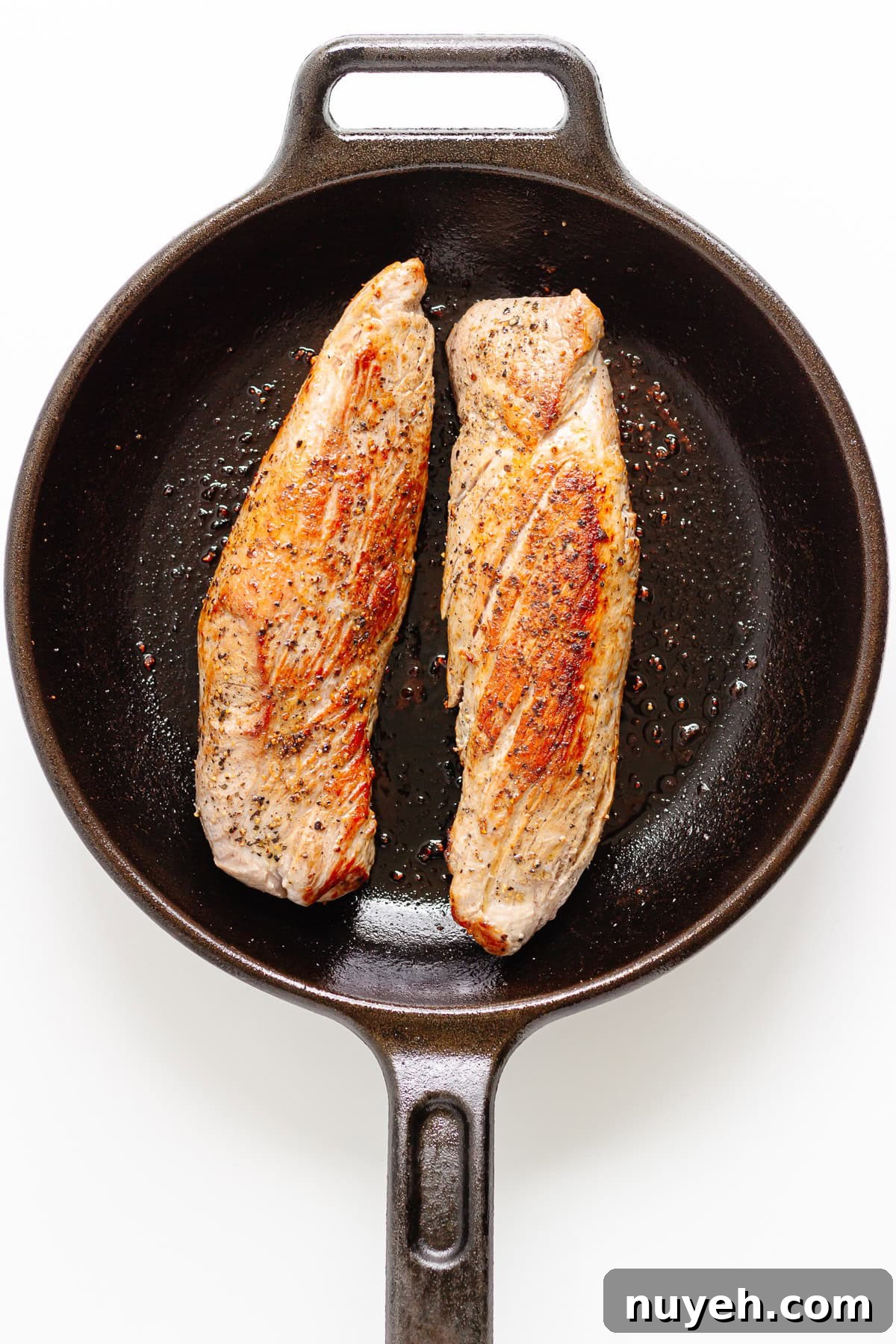 Two seared pork tenderloins in a cast iron skillet.