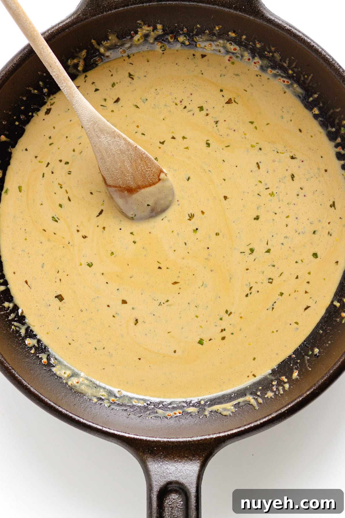 Creamy mustard pan sauce in a cast iron skillet with wooden spoon.