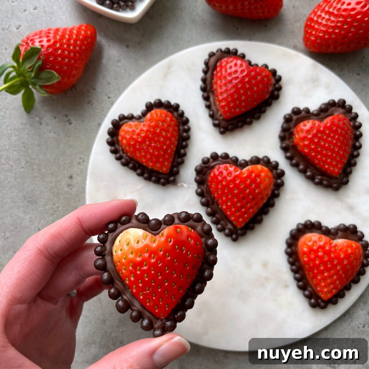 A hand holds a Strawberry Chocolate Heart with a chocolate dot border.