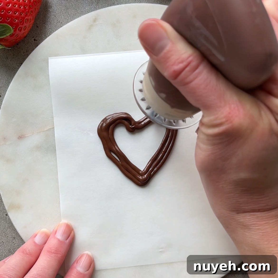 A hand pipes a dark chocolate heart.