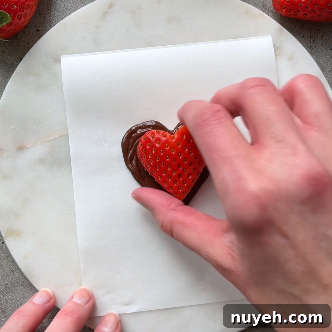 A hand places a strawberry heart on top of a dark chocolate heart.