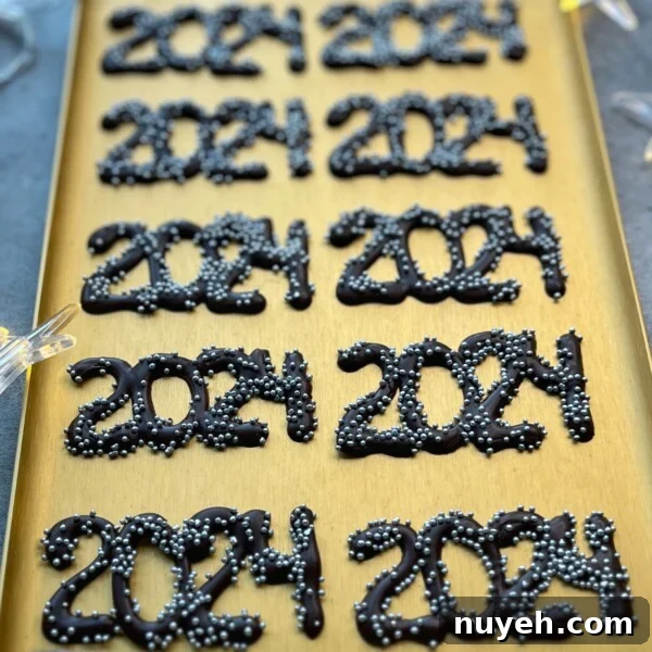 A gold tray displays several chocolate decorations shaped as “2024,” each topped with small silver sprinkles, perfect for adding a festive touch to your party bites or inspiring creative dessert recipes.