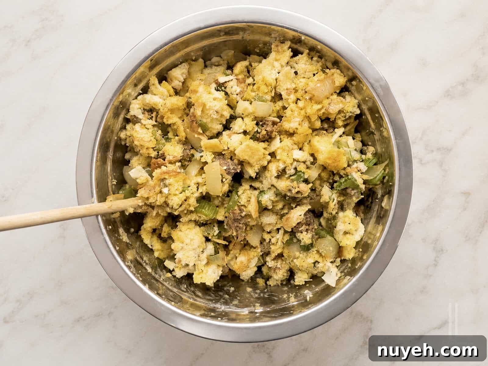 Close-up of a bowl of savory cornbread dressing with sausage and herbs being stirred together before baking.