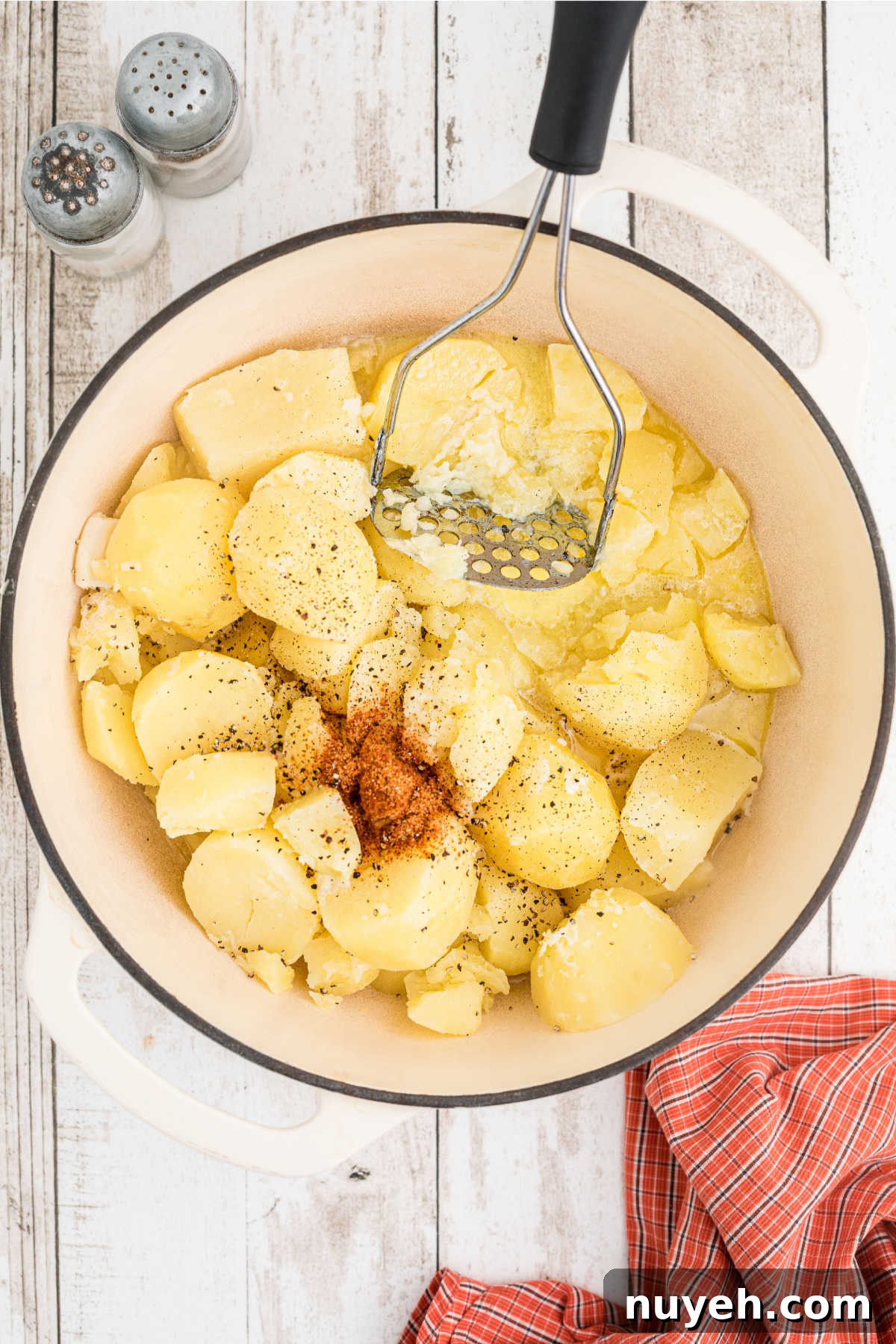 Potatoes about to be mashed with seasoning in a large pot.