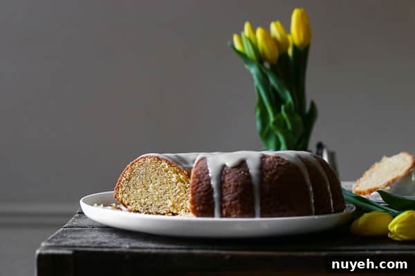 A cut bundt cake with icing dripping on a plate next to flowers