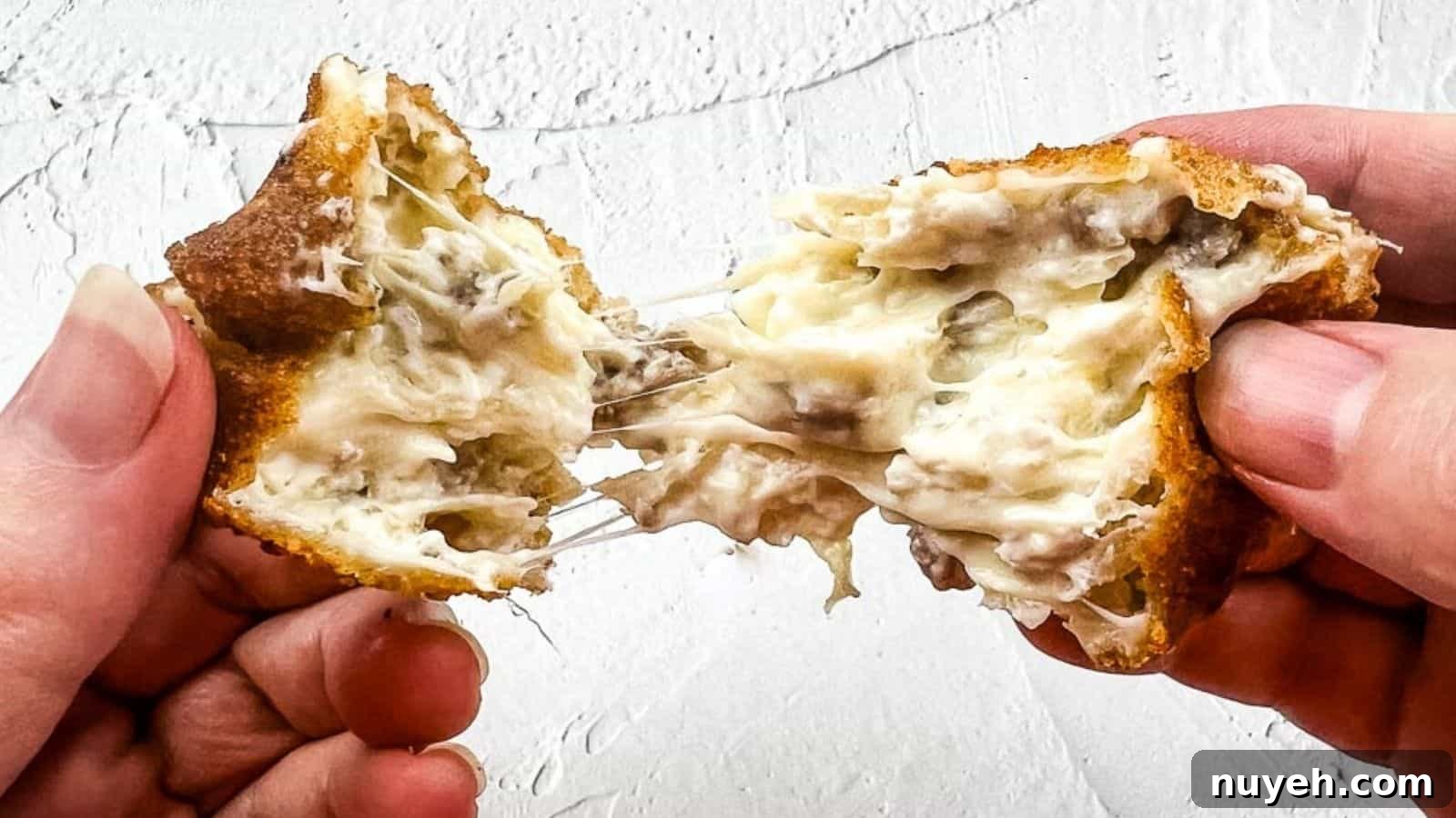 A close-up shot of hands pulling apart a crispy, golden-brown, cheese-filled snack with a gooey, melted cheese center against a textured white background.