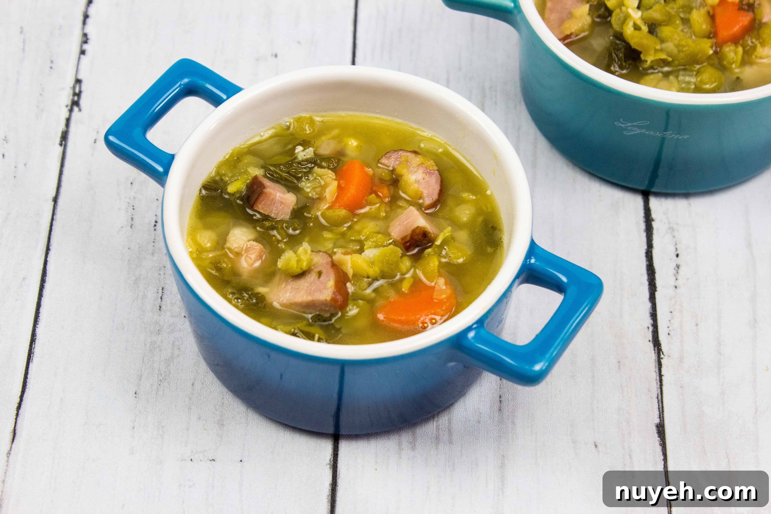 Two bowls of soup with ham, sausage, split peas and vegetables in them.