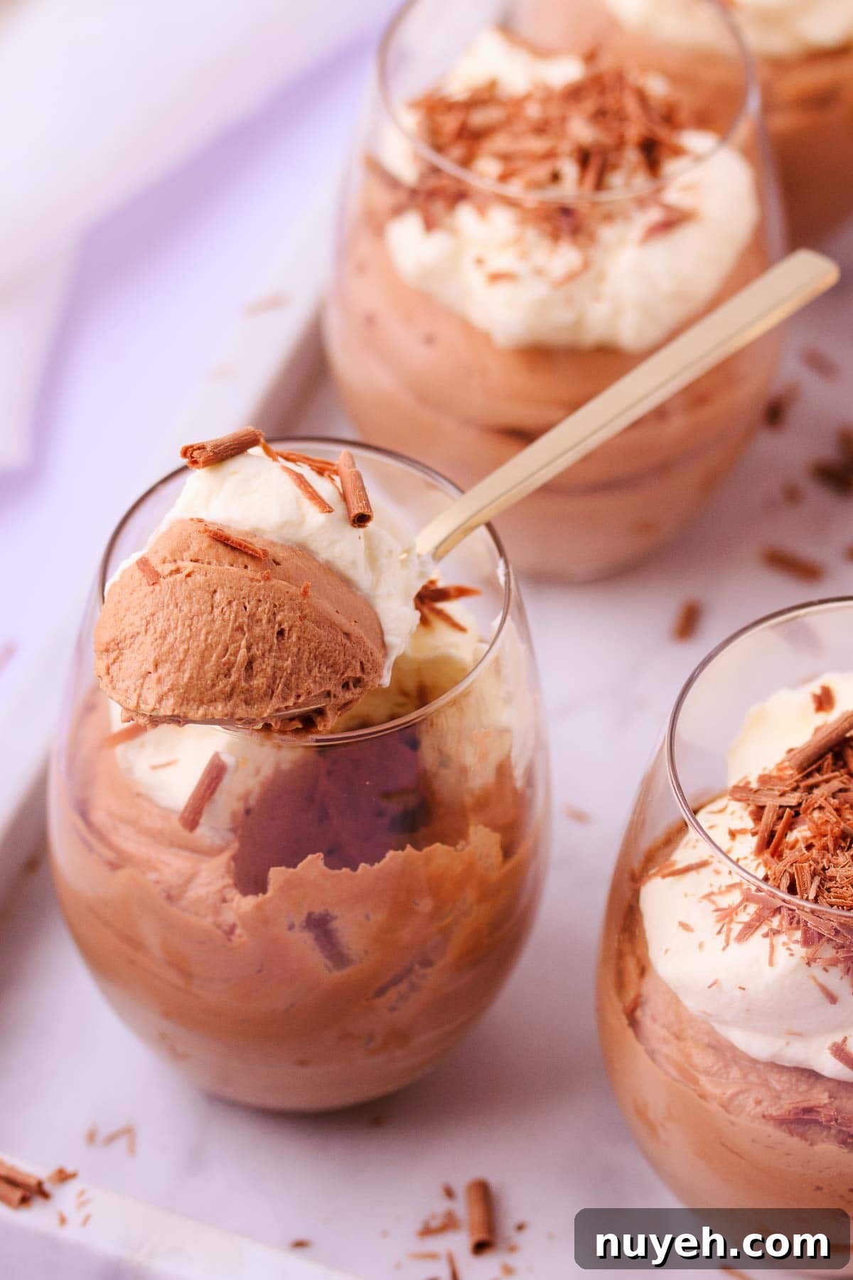 Close up of a spoonful of milk chocolate mousse resting on the rim of the glass, showing the fluffy mousse texture. 