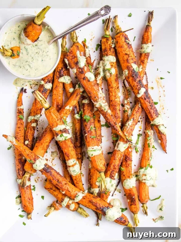 White platter with whole roasted and coated with spices carrots. A small glass bowl of dipping sauce with a few carrots in there and a spoon. The sauce is greenish and it's also drizzled on the cooked carrots. There are fresh herbs scattered around.