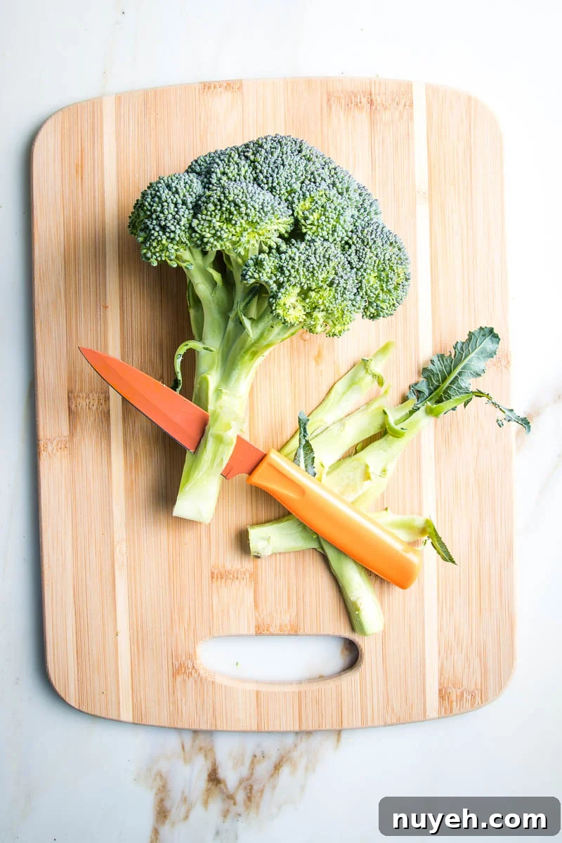 Paring knife cutting off the woody outer layer of a head of broccoli.