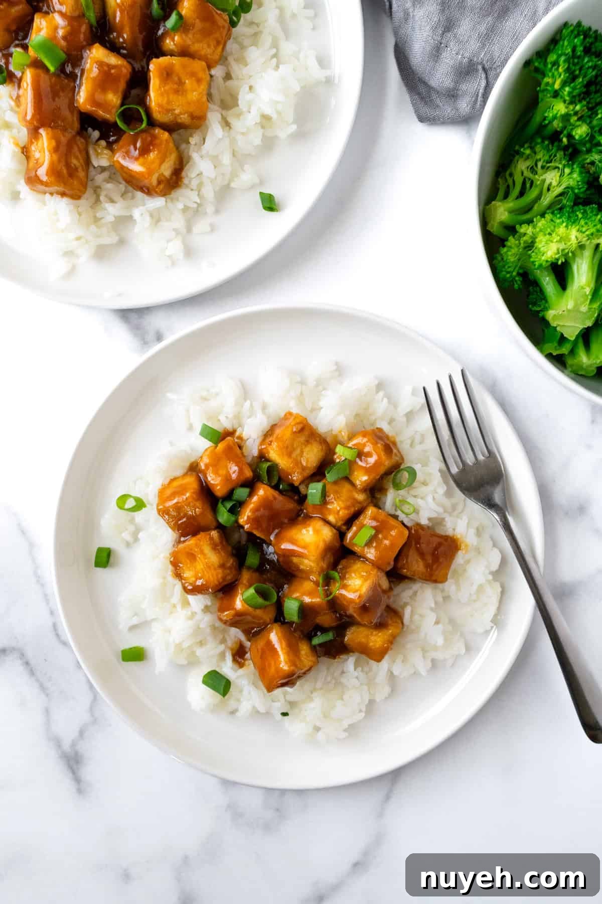 Crispy Orange Tofu Recipe with Sticky Citrus Glaze 2 Orange Tofu over white rice on a white plate with a fork.