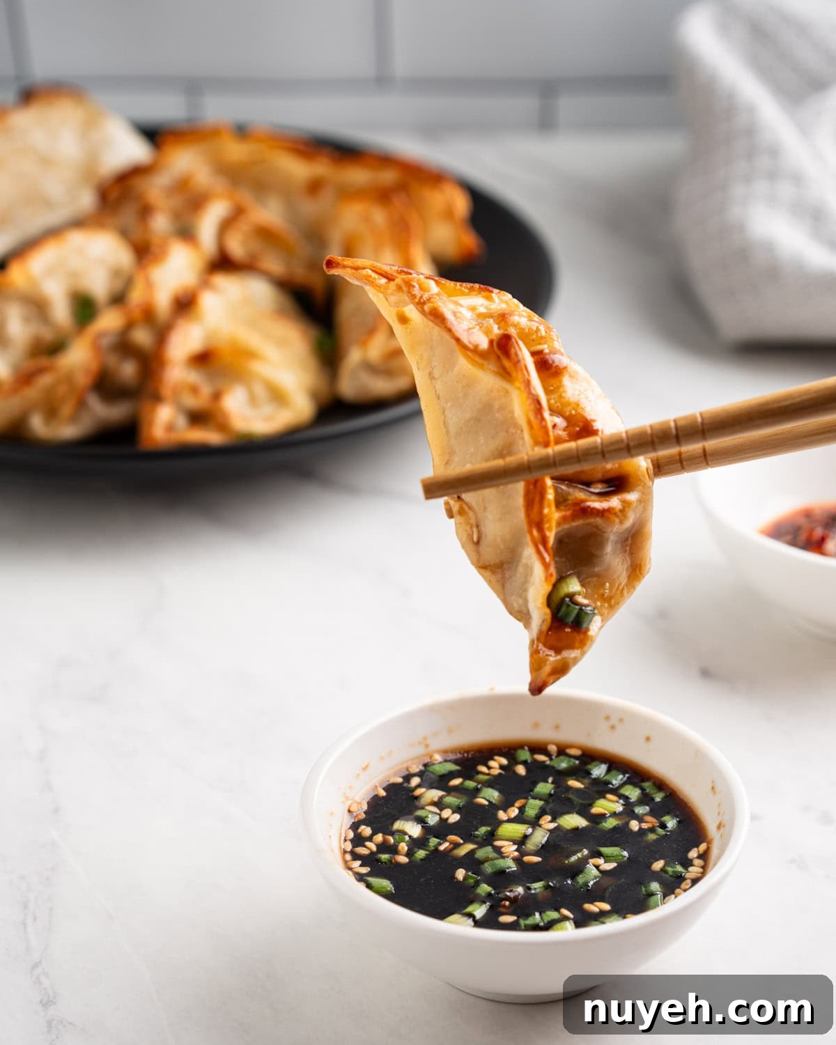 chopsticks dipping air fried dumplings into soy sauce.