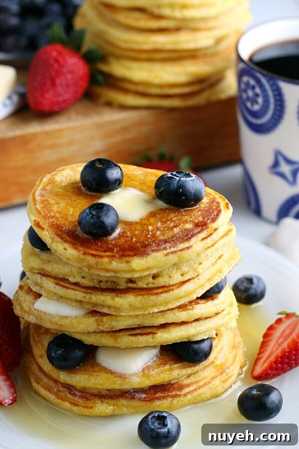 Fluffy Cornbread Pancakes Recipe with Honey Butter 5 A stack of cornmeal cakes with blueberries.
