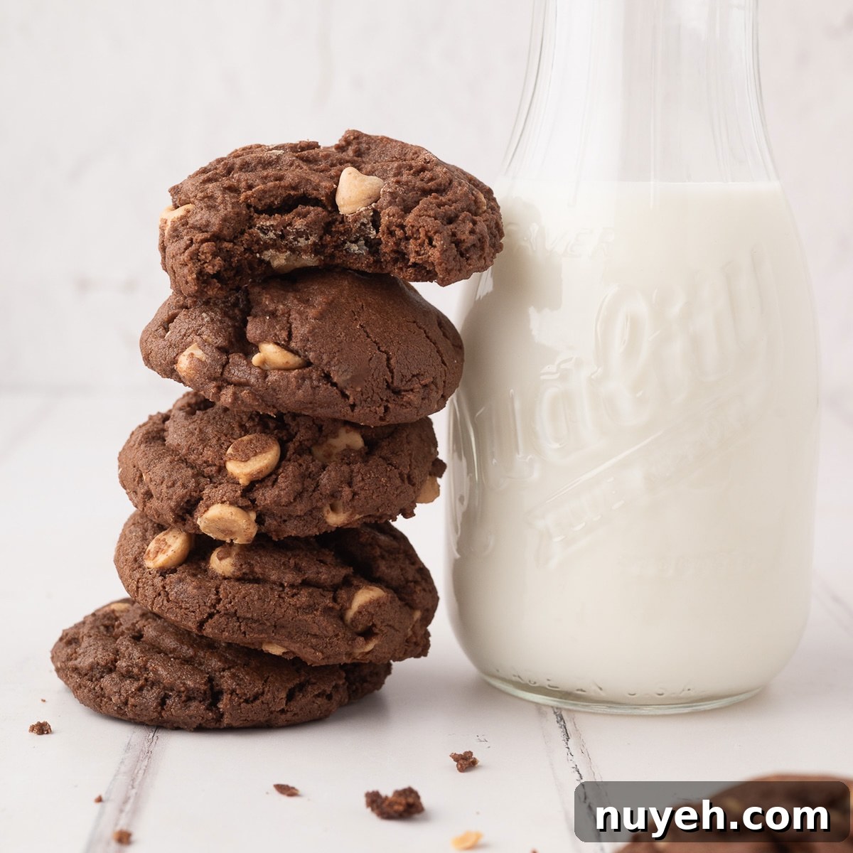 A tall, vertical stack of soft and chewy chocolate peanut butter chip cookies showing the rich cocoa texture and melted Reese's chips next to a vintage bottle filled with milk.