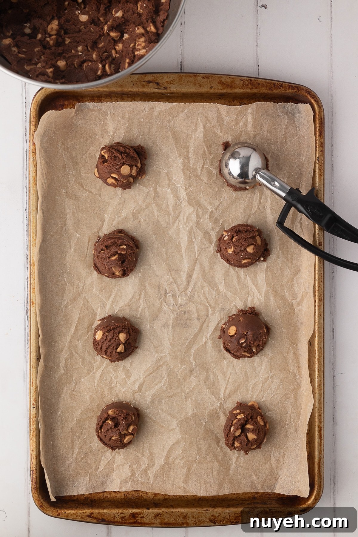 Using a standard-sized metal cookie scoop to portion out chocolate dough onto a parchment-lined baking sheet.